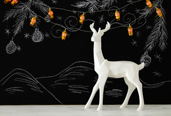 White reindeer on wooden table over chalkboard background with hand drawn chalk illustrations.