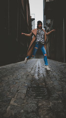Lifestyle full portrait of young attractive fashionable Caucasian female in a coat walking in the narrow street in Europe. Vertical photo