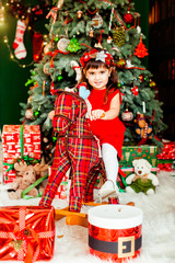 Littlle girl in red dress sits before a green Christmas tree in the room