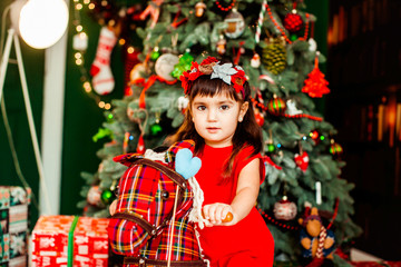 Littlle girl in red dress sits before a green Christmas tree in the room