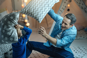 Positive delighted man playing with his son