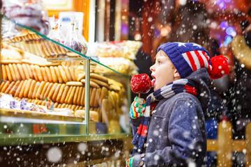 Little kid boy eating sugar apple sweets stand on Christmas market