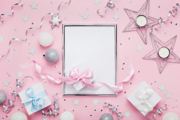 Christmas mockup with frame, holiday balls, gift boxes and sequins on stylish pink table top view. Fashion festive background. Flat lay.