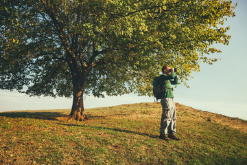 Man is watching nature with binoculars on sunny day.