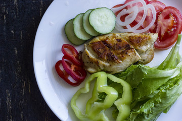 A fresh meal of chicken fillet with vegetables and tasty juice on a dark wooden background