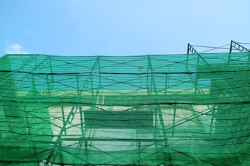 Construction scaffolding with green cover at the building. Copy space with blue sky background.