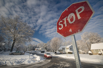 Beneath a stop sign, a red car turns on an icy, snowy street.
