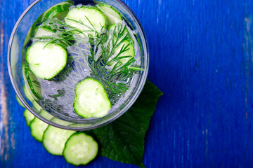 Cucumber water   in glass with dill on blue wooden background. Detox, diet. Top view. Copy space