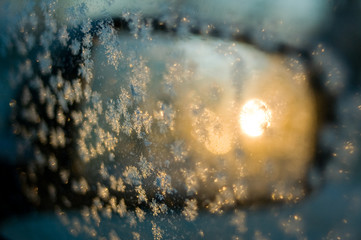 A car’s mirror reflects rising sun, illuminating snowflakes in its window.