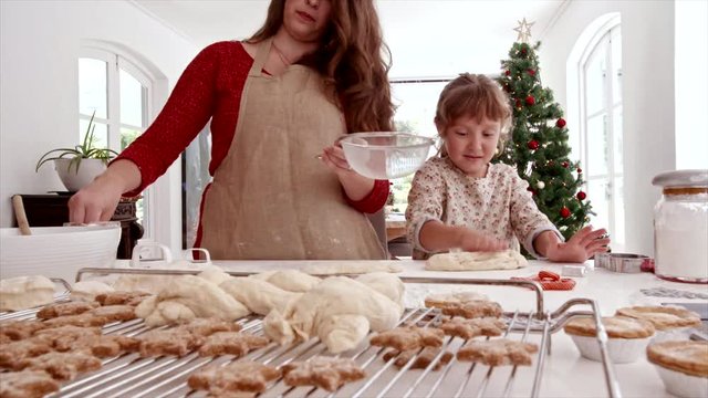 Smiling young woman with little girl sprinkling flour on dough. Mother and daughter preparing Christmas cookies.