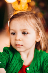 Little girl in green sweater poses before a Chirstmas tree in the room
