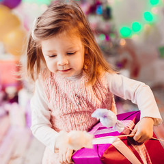 Little girl in pink dress plays in the room with pink Christmas tree