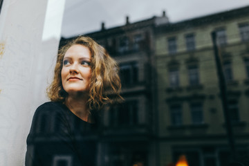 Junge blonde Frau schaut lächelnd aus dem Fenster