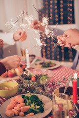 X mas noel miracle, holy spirit! Close up cropped shot of gathered relatives, setted festive desktop with tasty treats plates, mealth of healthy food, arms putting sticks of sparklers together