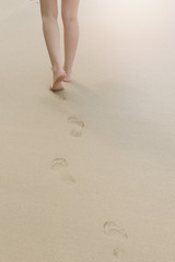 back view of woman walking on sand beach leaving footprints in the sand. 
