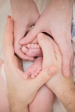 Baby's feet in mom's and dad's hands. Happy young family.
