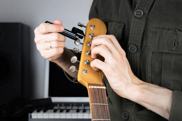 Changing electric guitar strings. Male hands using guitar tuning peg winder to set up new strings...