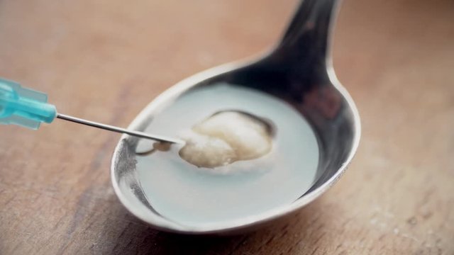 Dirt heroin is filtered with cotton on a needle in a glass syringe. 4k UltraHD video footage.
