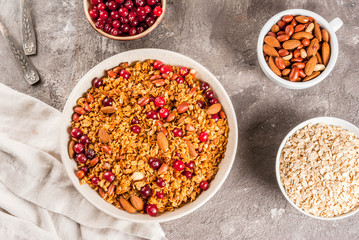 Ideas for a winter, autumn breakfast. Thanksgiving, Christmas. Homemade fresh cooked honey granola with nuts (almonds, peanuts, hazelnuts) and cranberries. On gray concrete table, Copy space top view