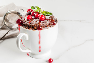 Winter, fall healthy breakfast or snack. The idea of a quick treat for Christmas. Chocolate mug cupkake in ceramic cup, with cranberry and sauce, powdered sugar. White marble table, copy space