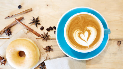 Hot coffee heart in blue cup and donut on wooden