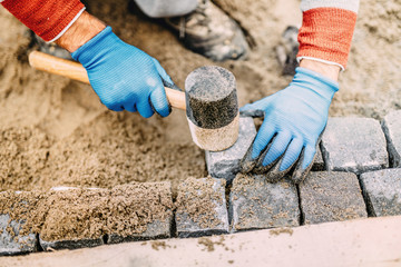 Construction worker placing stone tiles, cobblestone blocks in sand. Portrait of industrial worker