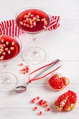 Creamy vanilla panna cotta with red jelly in beautiful glasses, fresh ripe pomegranate on white wooden background.