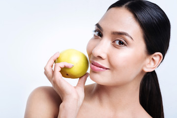 Pleasant dark-haired woman holding apple near her face