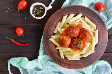 Penne pasta with meat balls in tomato sauce in a clay bowl on a dark wooden background. Top view.