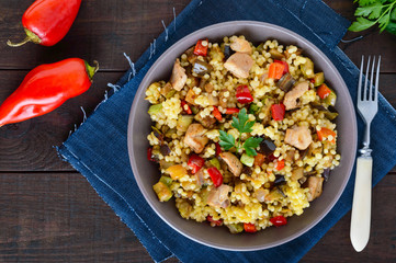 Light healthy dietary salad with couscous, vegetables (zucchini, eggplant, carrots, sweet peppers, onions), chicken pieces on a dark wooden background. Top view.
