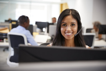 Young woman working at computer with headset in busy office