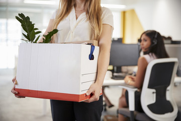 Fired female employee holding box of belongings in an office - obrazy, fototapety, plakaty