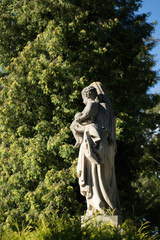 gray mother and child gravestone surrounded by greenery and warm sunshine shining from behind the trees