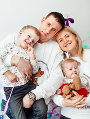 Mom and dad sit with thier two little sons in a pink room with Christmas tree