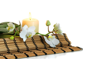 Spa combination with orchid flowers, burning aromatic candle and a bast mat isolated against white...
