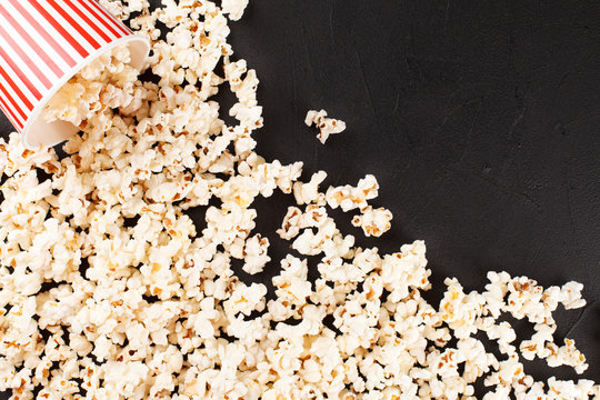 Popcorn horizontal banner. Red stripped paper cup and kernels lying on dark background. Copy space.