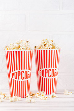 Popcorn vertical banner. Red stripped paper cup and kernels staying on white wooden background. Copy space.