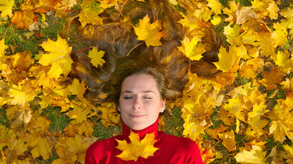 Naklejka na ściany i meble Woman with stretched hair lying on leaves in a park in autumn (1)