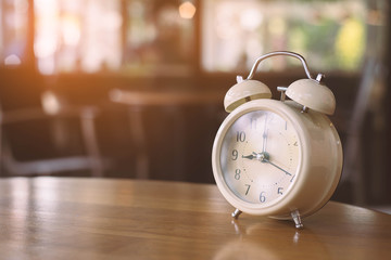 Vintage alarm clock on wooden table in the coffee shop.