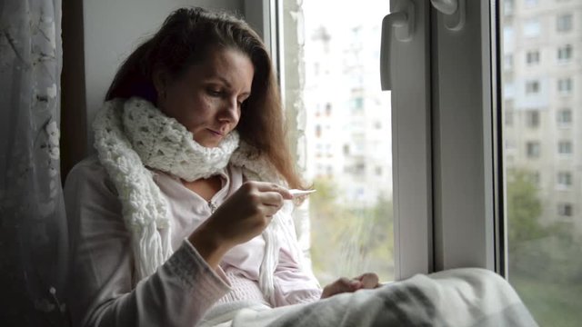 A woman is sick, she measures the temperature of the body, at the window