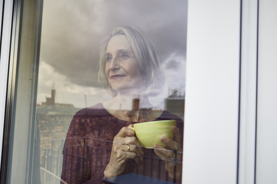 Mature woman holding coffee mug looking out of window