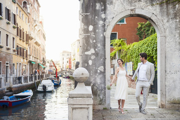 Italy, Venice, bridal couple walking hand in hand through archway