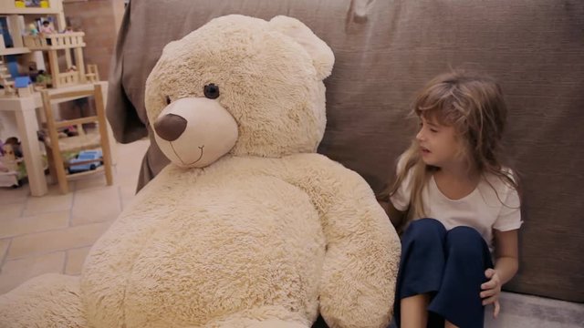 A cute little girl crying and seeking a hug from her toy friend, a giant teddybear.
