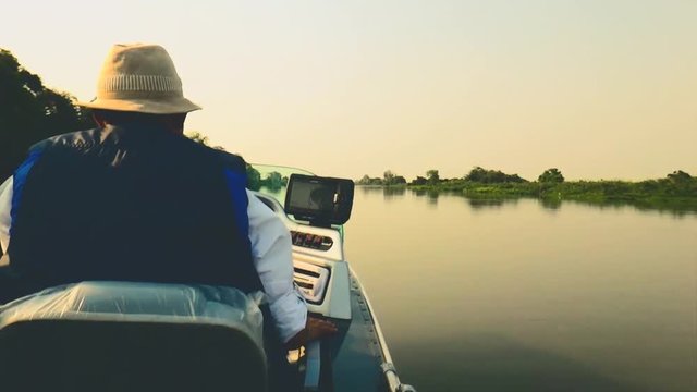 Fisherman navigating in his boat on calm waters at sunset on Paraguai river, in Pantanal - Brazil. 