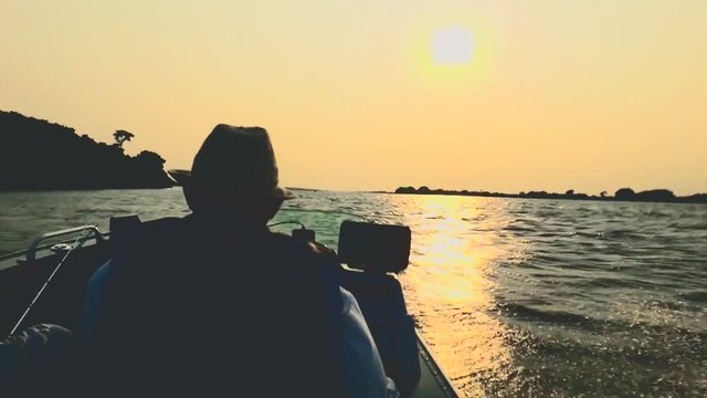 Silhouette of a fisherman navigating in his boat on a windy day at sunset on Paraguai river, in Pantanal - Brazil. Boat jumping on waves from the constant wind. Sunset and the sun reflecting on water.