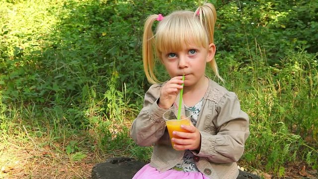 Beautiful little girl drinking orange juice outdoors