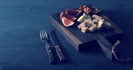 Blue cheese, fresh figs and walnuts on a wooden Board and a knife and fork