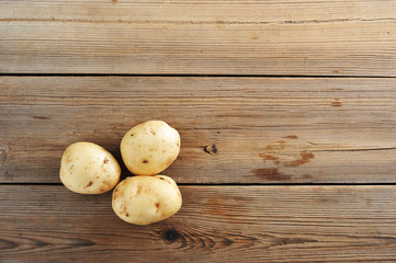 Three young tuber raw white potatoes on rustic wooden background