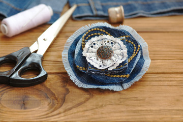 Creative things to do with old jeans. Handmade denim flower brooch. Scissors, thread, thimble, needle, female old jeans on a wooden background. What to do with torn jeans. Closeup