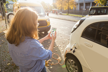 Woman with phone on a background of electric cars charging point. E-car sharing concept